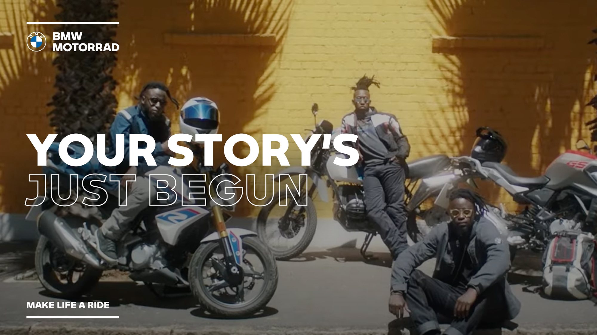Three riders with their BMW Motorrad motorcycles against a yellow wall: Your story's just begun. Make life a ride.