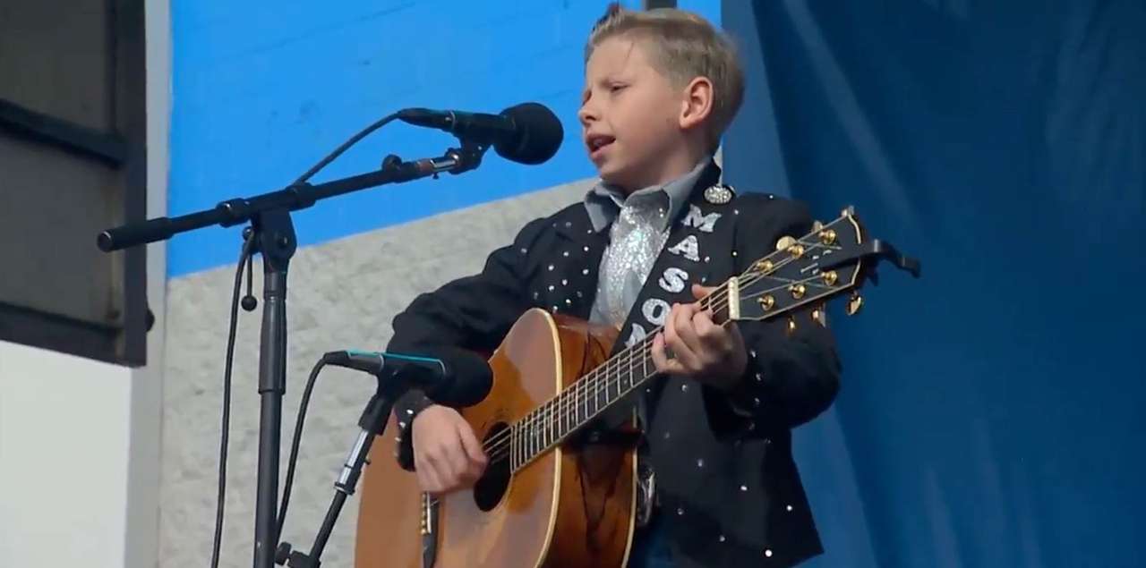 Mason Ramsey singing and playing guitar on stage at the live Walmart Yodel Boy event